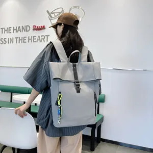 Detail view of a minimalist grey roll-top backpack worn in an indoor lifestyle cafe scene.