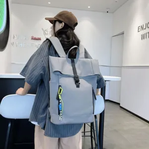 Detail shot of a minimalist grey rolltop backpack with black straps and a stylish keychain pendant.