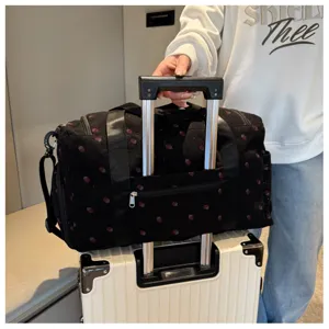 Black strawberry print travel duffel bag detail showing trolley sleeve and handles.