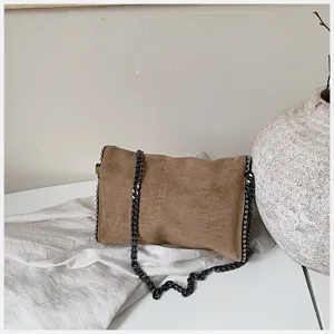 Bolso bandolera de ante marrón en detalle con cadena metálica y textura suave.