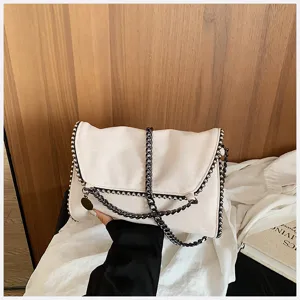 Bolso cruzado tipo sobre de ante con cadena metálica y bordes elegantes para la moda de invierno.