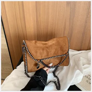 Vista detallada del bolso bandolera de ante marrón, diseño de sobre elegante con cadenas.