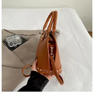 Bruine lederen schelp handtas zijkant detail met klinknagels, compacte retro tas.