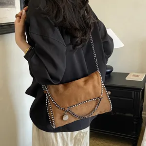 Elegante bolso bandolera de ante marrón con cadena elegante y abalorios metálicos.