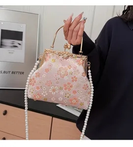 Vintage geborduurde bloemen schelp handtas met metalen handvat en elegante parelketting.