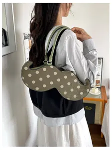 Detail shot of a unique mustache-shaped shoulder bag with polka dots and green handles.