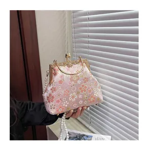 Gedetailleerd overzicht van roze bloemen geborduurde handtas met elegante parelketting riem.