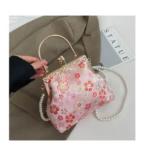 Roze geborduurde handtas met bloemen en kusslot met parelketting en metalen handvat.