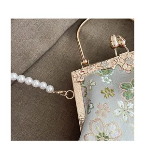 Close-up van geborduurd stoffen handtasdetail met metalen sluiting en parelketting.