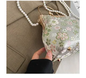 Detail van geborduurde bloemen schelp handtas, vintage knipsluiting met parelketting.