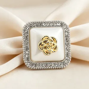 Primo piano di anello per sciarpa in seta quadrata con strass e camelia dorata.
