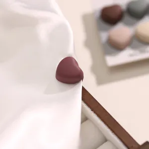 Close-up detailgezicht van een donkerpaarse hartvormige magnetische broche op witte stof.
