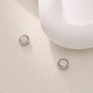 Nahaufnahme kleiner runder magnetischer Hijab-Clips auf strukturiertem weißem Hintergrund, Detail.