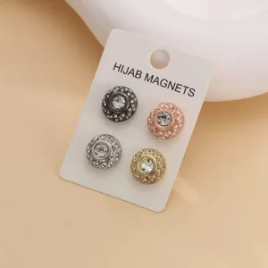 Vista dettagliata di quattro spille magnetiche con strass per hijab in varie finiture su carta.