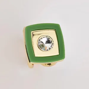Detail view of a square green acrylic and gold metal scarf ring with a sparkling crystal.