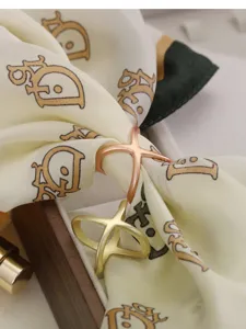 Detail view of stylish metallic X-shaped scarf buckle in rose gold and matte gold finishes.