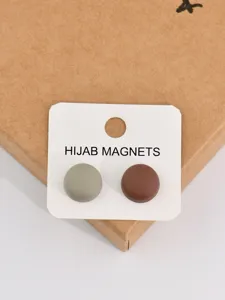 Close-up of circular magnetic hijab pins set in two colors on white card and box.