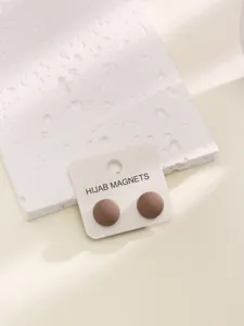 Primo piano dettagliato di magneti hijab marroni opachi rotondi su cartoncino, sfondo minimal.