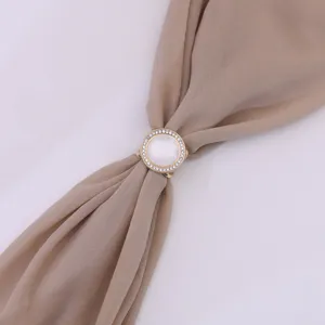 Close-up van een goudkleurige ronde strass sjaalgesp met witte inleg voor elegante dagelijkse mode.