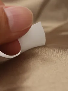 Detail shot of invisible anti-slip double-sided clothing tape peeling off backing.
