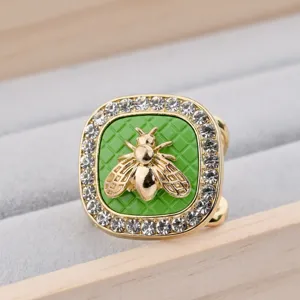 Close-up detail of a square scarf buckle with rhinestone border, green grid and gold bee accent.