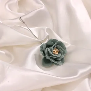 Primo piano dettagliato di un'elegante spilla con rosa in tessuto grigio-verde su seta.