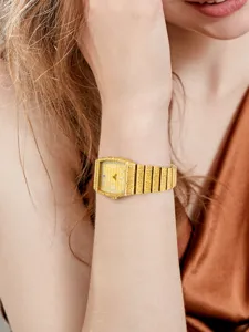 Montre quartz femme carrée dorée de luxe avec index diamant, chiffres romains et bracelet texturé.