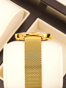 Primer plano detallado del reloj de cuarzo dorado de lujo con correa de malla fina y caja.