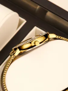 Primer plano detallado de reloj de cuarzo dorado para mujer con bisel de estrás y malla.