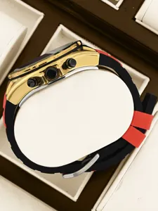 Vista detallada del reloj cronógrafo dorado con correa de silicona negra y roja.