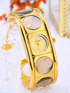 Close-up detail of the gold wide cuff quartz watch with circular transparent accents.