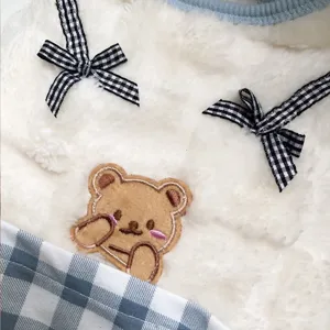 Detail shot of fluffy pet vest featuring cute plaid bows and embroidered bear patch texture.