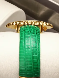 Detail view of women luxury emerald watch with green leather strap and gold case chic design.