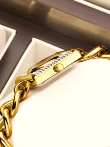 Primer plano de reloj de mujer rectangular dorado con pedrería y detalle de correa de cadena.