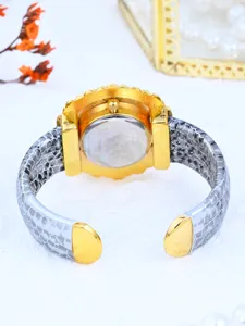 Gold cuff watch with grey snakeskin pattern strap, elegant detail view of women timepiece.