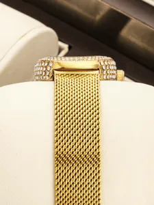 Primer plano detallado del reloj dorado para mujer con pedrería y correa de metal.