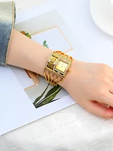 Primer plano detallado de la esfera del reloj pulsera dorado y correa de jaula con pedrería.