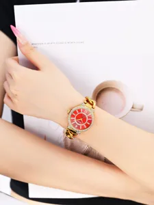Vista detallada de reloj de cuarzo dorado para mujer, esfera roja y bisel de pedrería.