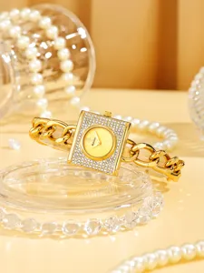 Vista en detalle del lujoso reloj dorado cuadrado con pedreria y elegante correa de cadena.