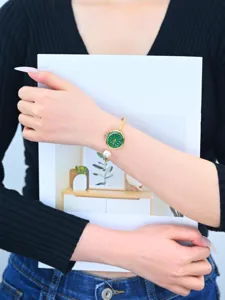 Elegante orologio rigido da donna con quadrante verde, ciondolo di perla e cinturino oro.