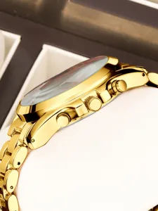 Détail latéral de montre chronographe dorée, bracelet en métal, couronne et poussoirs.