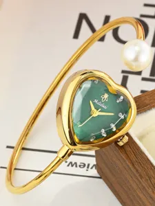 Close-up detail of the luxury gold bangle watch featuring a stylish green heart dial and pearl.