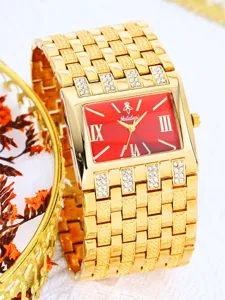 Detalle reloj mujer dorado, esfera roja rectangular con números romanos y brillantes pedrerías.