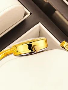 Close-up detail of luxury gold bangle watch crown and metal strap in velvet display case.