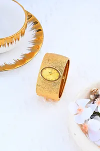 Detalle exquisito de reloj dorado con brazalete texturizado y esfera ovalada elegante.