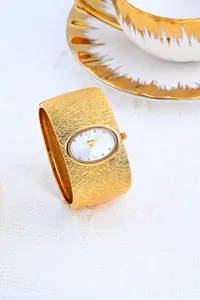Reloj de pulsera rígida dorado de lujo con esfera blanca ovalada elegante y diseño texturizado.