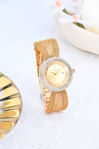 Close-up of luxurious gold women's watch with rhinestone bezel, mesh strap and calendar dial.