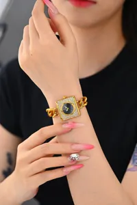 Detalle de reloj cuadrado de lujo con pedrería, correa de cadena elegante y movimiento de cuarzo.
