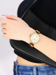 Detalle de reloj de cuarzo con pedrería dorada, esfera elegante y correa de cadena.