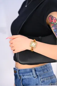 Primer plano de reloj cuadrado dorado con pedrería y correa de cadena gruesa, elegante para mujer